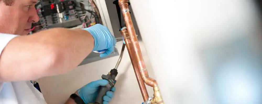 Water heater repair technician testing copper pipe connections and controls in Greenville, NC